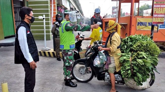 					Petugas TNI dari Koramil 12/Mranggen memeriksa suhu tubuh warga yang akan masuk ke dalam Pasar Mranggen, Demak, Rabu (6/1/2021). ()