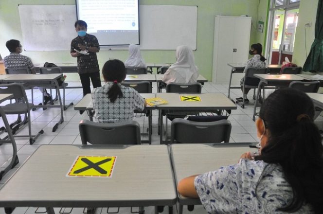 					Suasana pembelajaran tatap muka dengan menerapkan protokol kesehatan yang ketat. Setiap meja yang kosong diberi tanda silang.