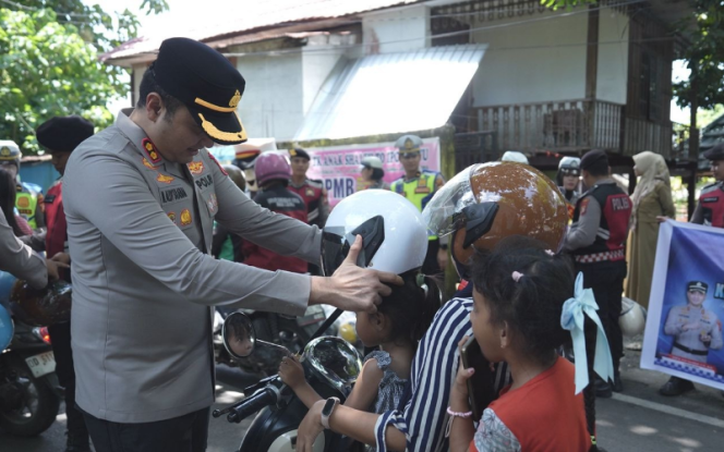 					Kapolres Gowa memasangkan helm kepada pengendara anak saat pembagian 100 helm gratis sebagai upaya meningkatkan kesadaran keselamatan berlalu lintas. Foto: Ist 